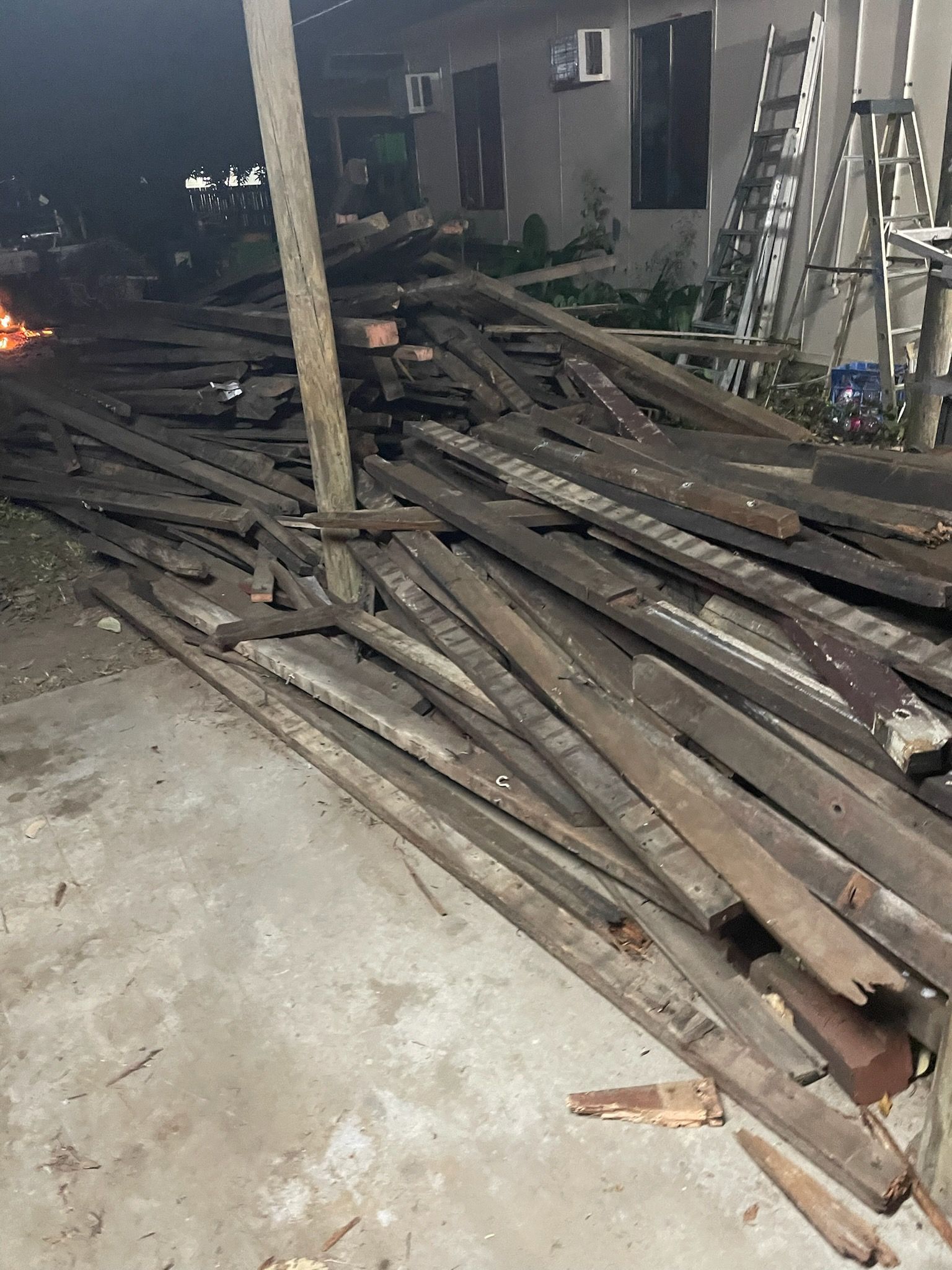 Stack of bricks on a wooden pallet, in a dirt lot. Houses and a fence are in the background.