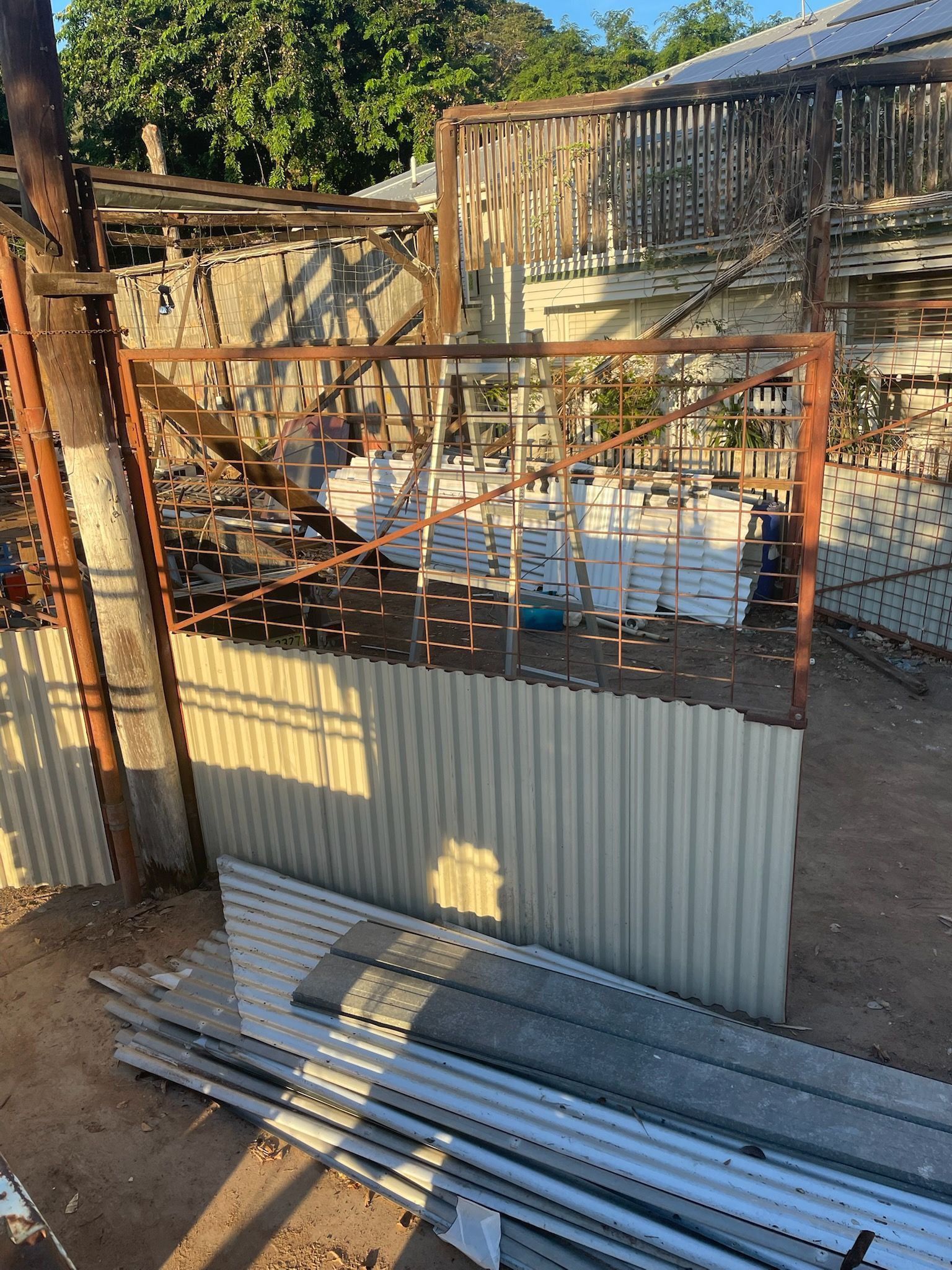 Rusty metal gate and fence in an outdoor storage area. Corrugated metal siding is visible.