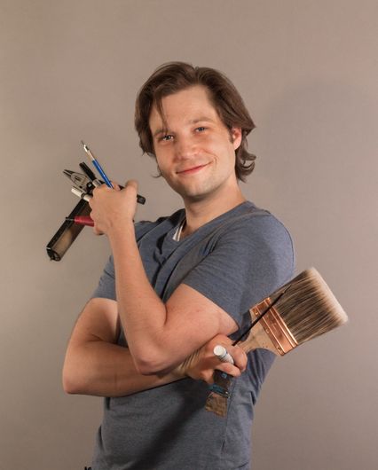 Artist Garubba holds tools of his trade: brushes, rollers, gouges, and pencils.
