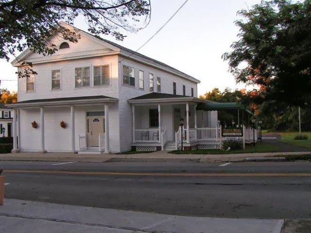 White two-story house with a covered porch beside a street at dusk