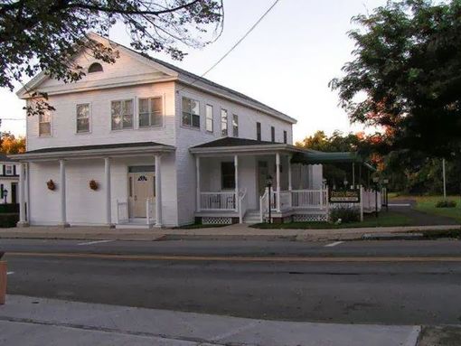 White two-story house with a covered porch beside a street at dusk