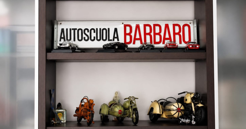 Insegna Autoscuela BARBARO sopra uno scaffale di piccole motociclette o caschi