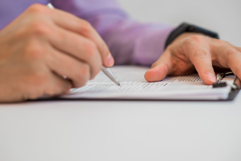 Mani che scrivono su un quaderno con una penna su un tavolo bianco.