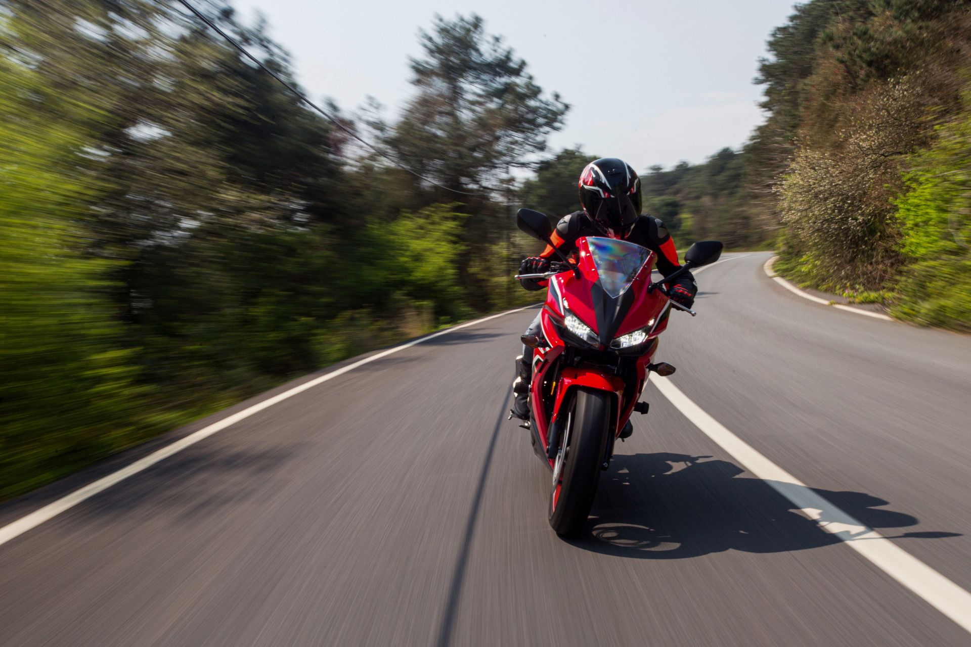 Motocicletta rossa inclinata su una strada tortuosa, pilota in tenuta nera, alberi ai lati della strada.