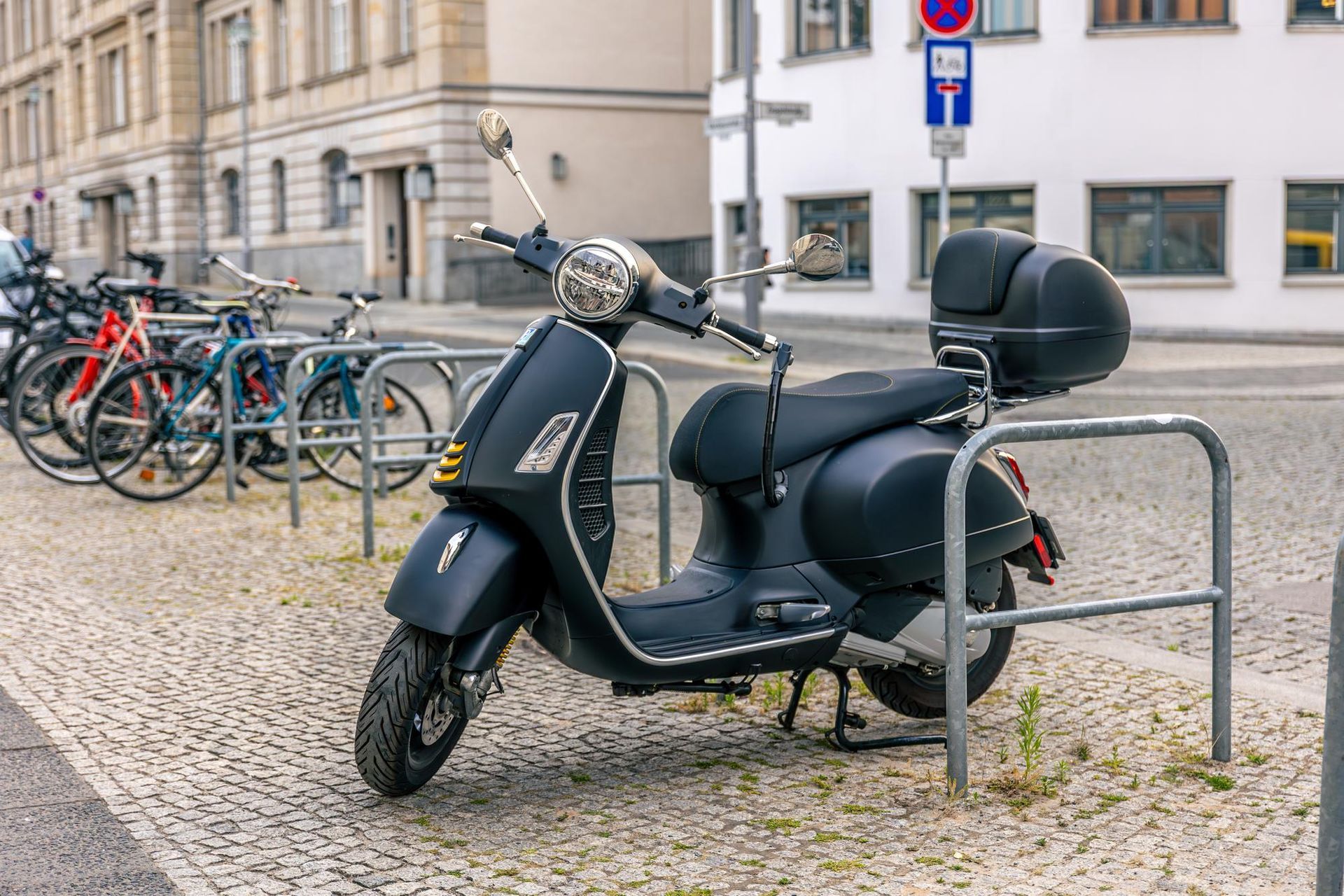 Scooter nero parcheggiato su una strada acciottolata accanto a rastrelliere per biciclette e un edificio