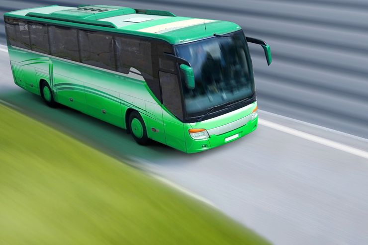 Autobus verde che percorre una strada curva, visto dall'alto.