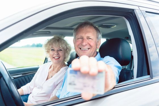Coppia sorridente in auto, l'uomo tiene in mano un biglietto rivolto verso il finestrino.