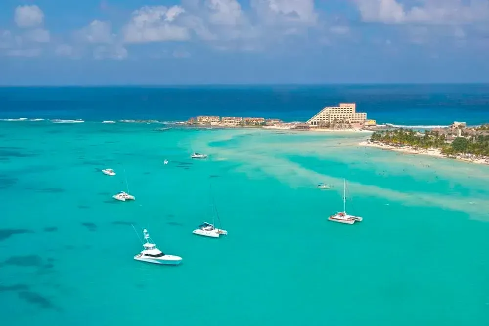 Beachfront resort with tall white building, pools, beach, and turquoise water.