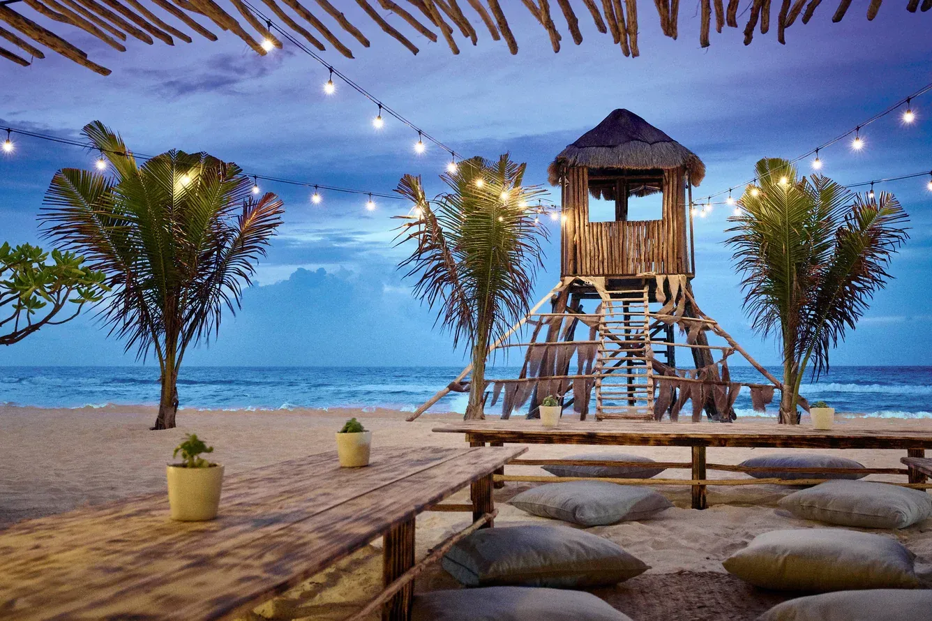 Resort pools and beach at dusk; ocean, thatched roofs, hotel.