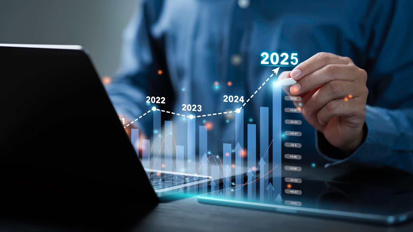 Persona dibujando un gráfico de tendencia ascendente en una pantalla holográfica, con una computadora portátil en primer plano; 2025 está en la cima.