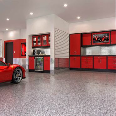 Red sports car parked in a luxury garage with red cabinets, stainless steel backsplash, and a television.