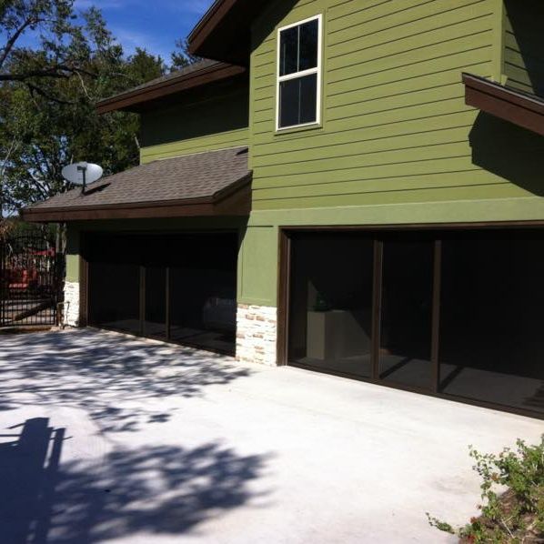 Green two-story house with screened patios and a paved driveway in sunlight