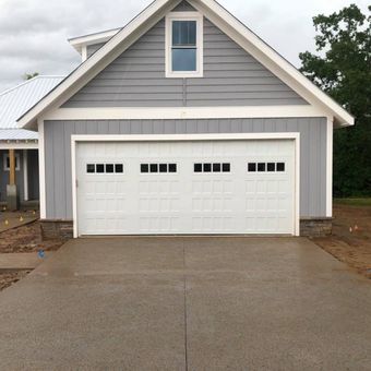 White garage door with black decorative hardware; above, a brick section and light siding.