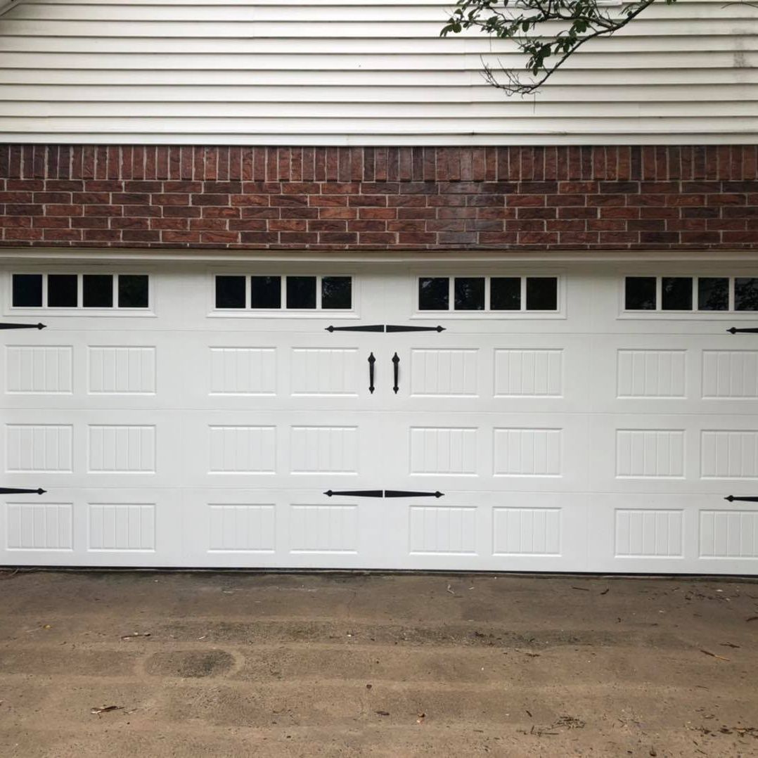 White garage doors under a brick and siding exterior with small windows above each door