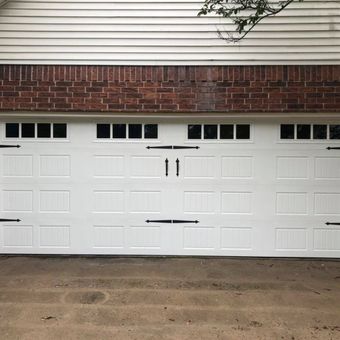 White garage door with black decorative hardware; above, a brick section and light siding.