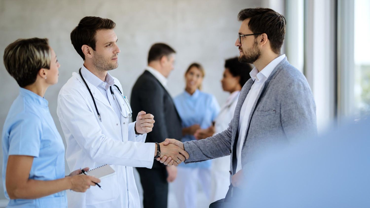 A doctor and a businessman are shaking hands in a hospital.