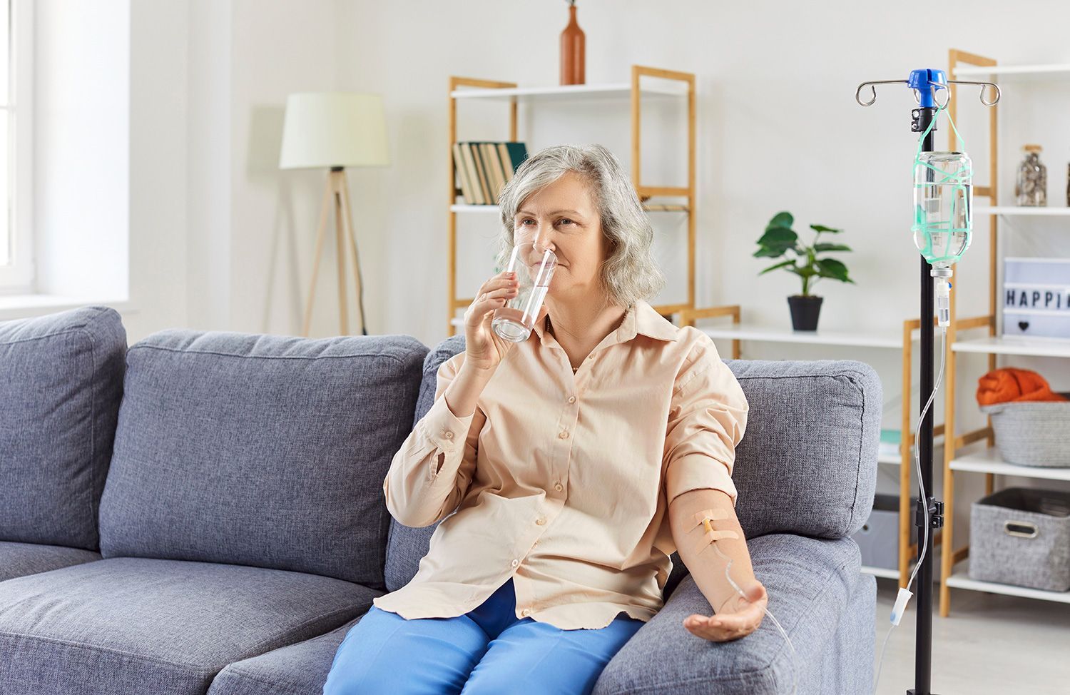 Older adult sitting on a gray sofa using a nasal inhaler in a bright living room