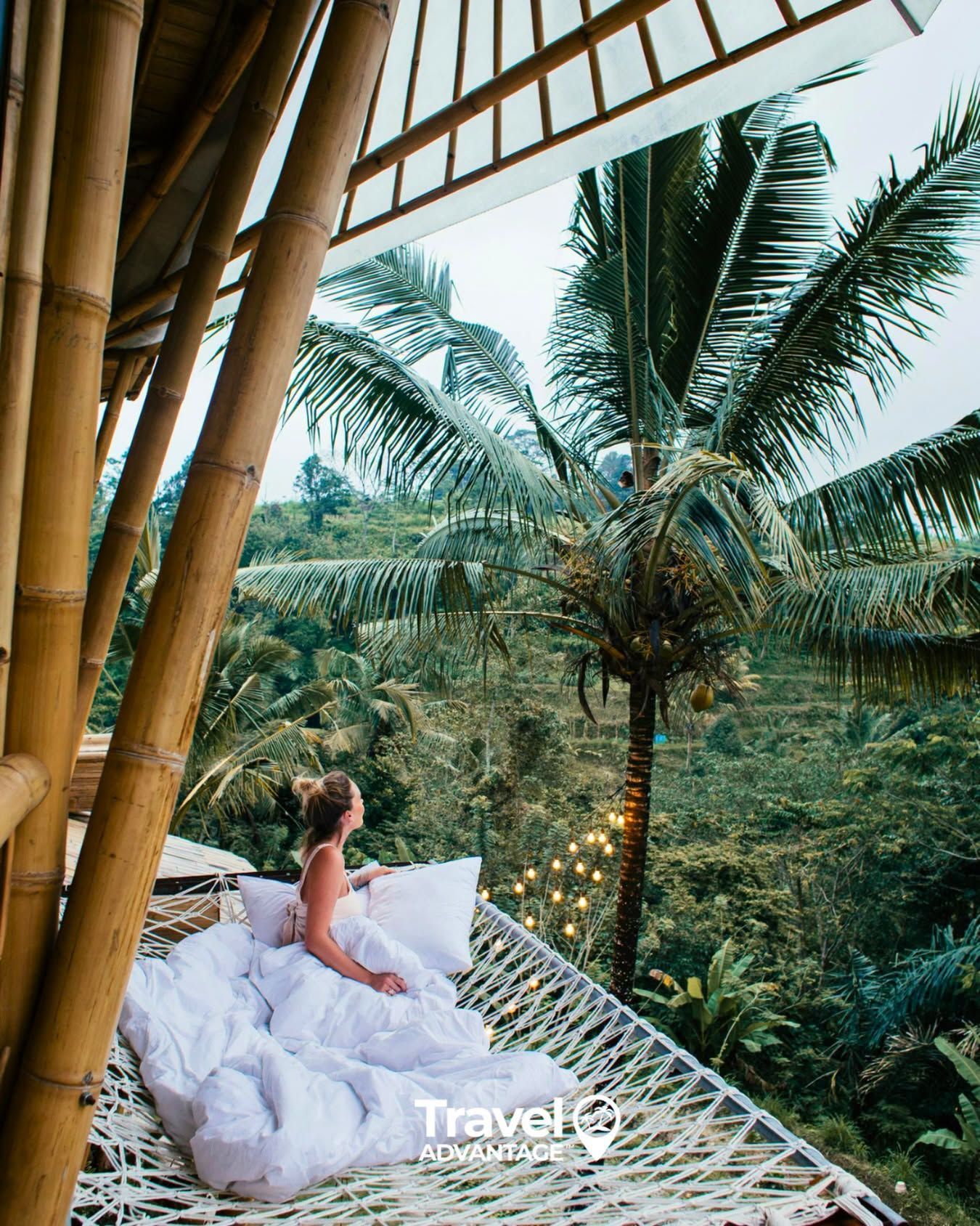 Woman in white sitting on a rooftop lounge overlooking lush palm trees at sunset