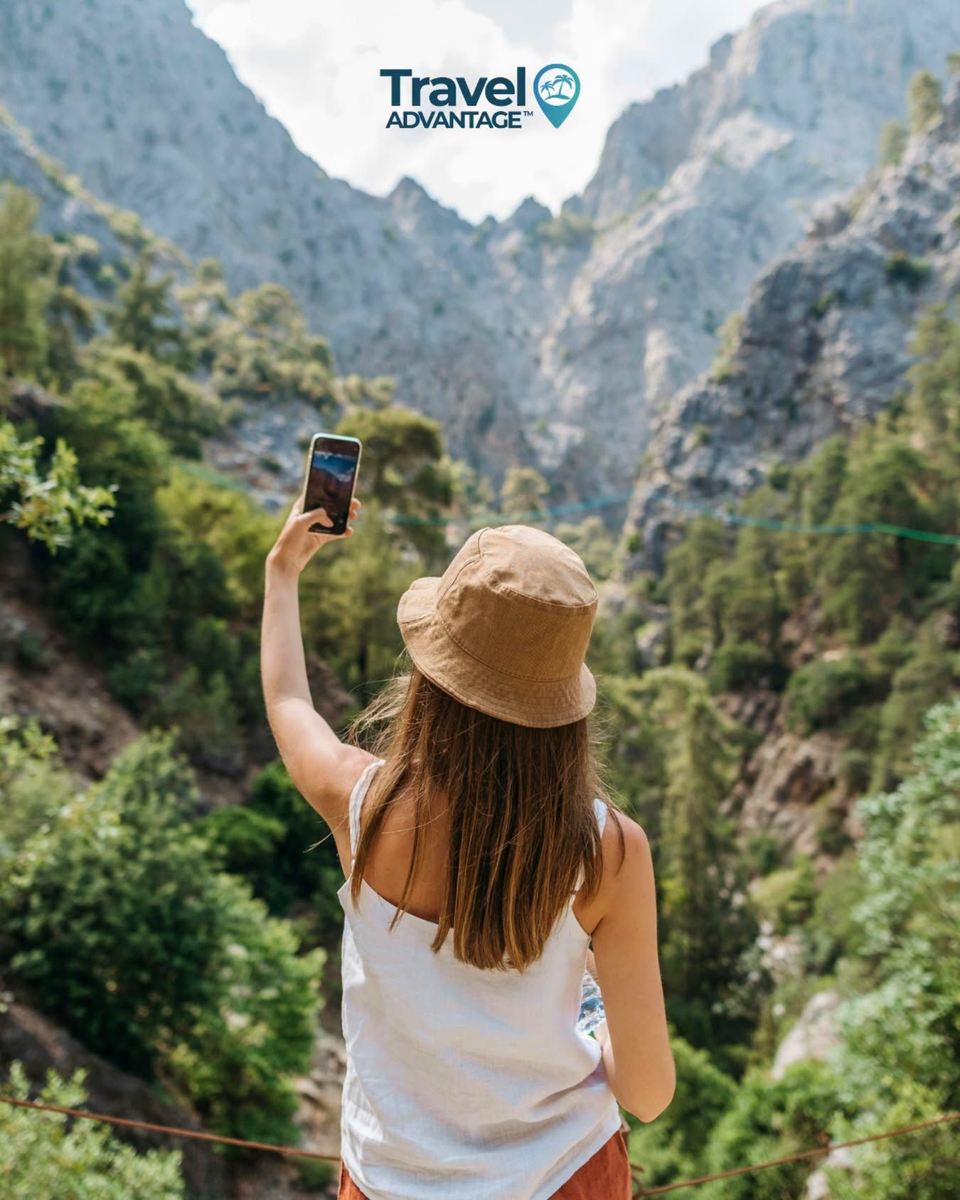 Traveler photographing a mountain valley, wearing a straw hat and white top, with steep cliffs ahead.