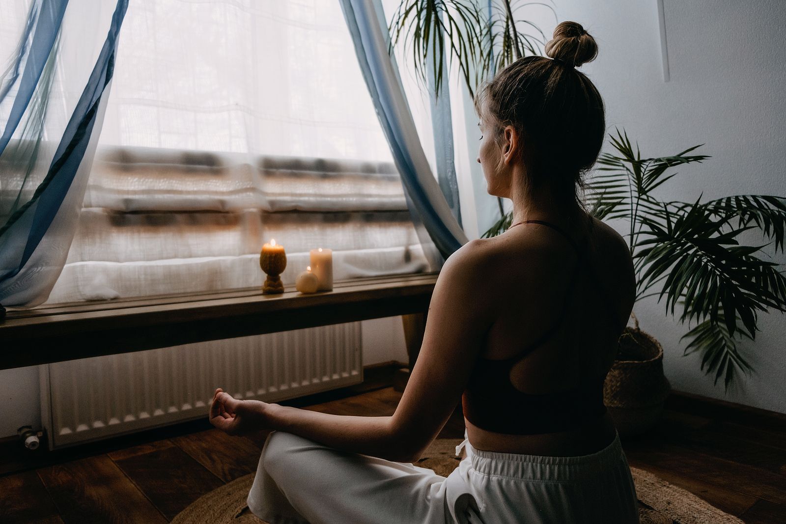 A woman is sitting in a lotus position in front of a window.