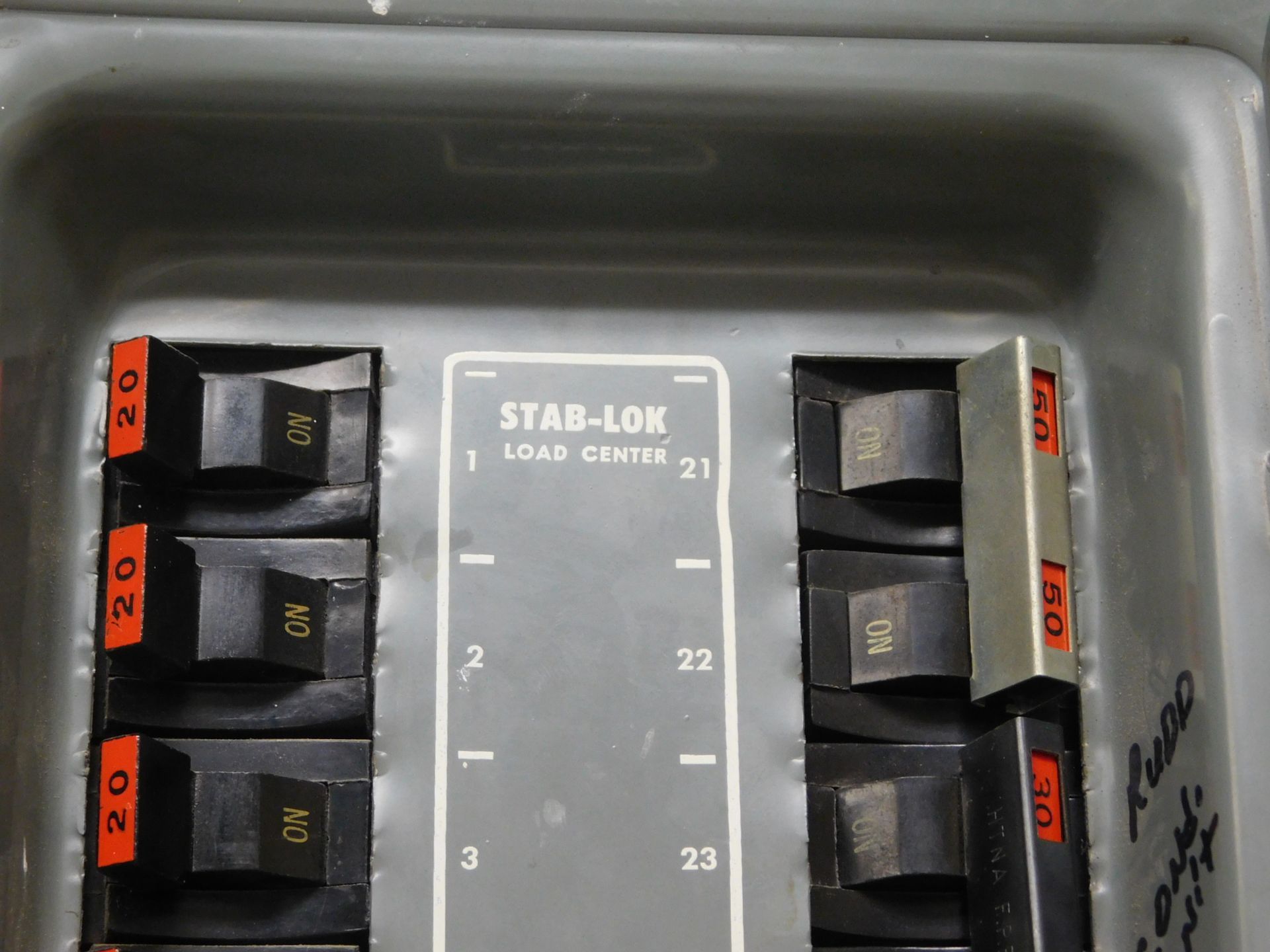 Electrical breaker panel with labeled black switches and orange tags inside a gray box