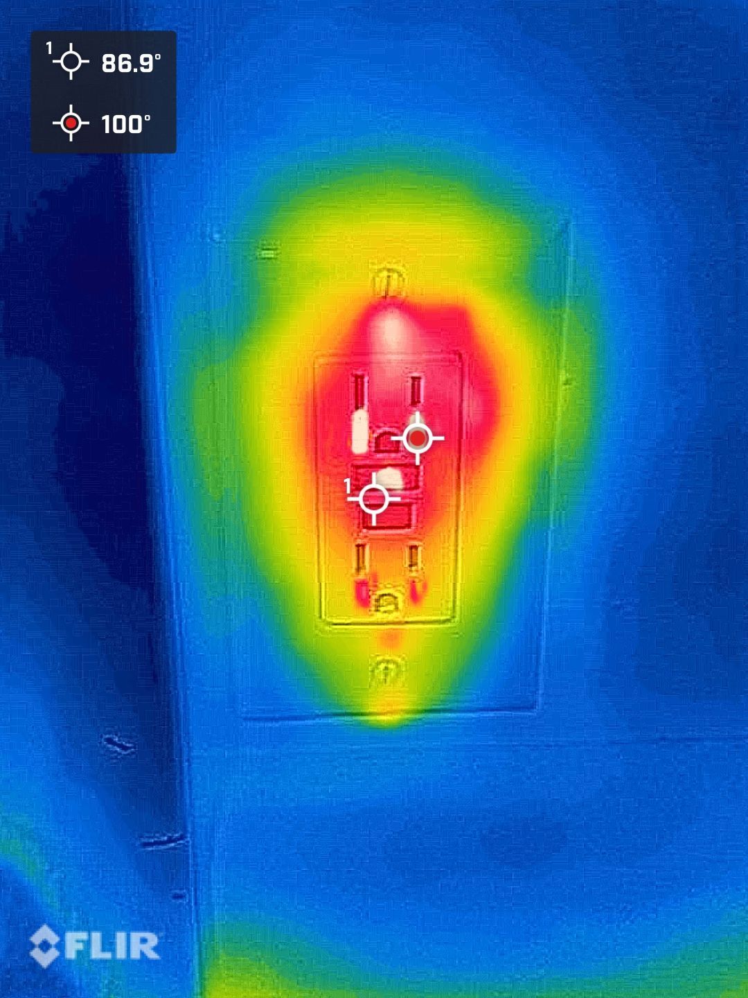 Thermal image of a wall outlet glowing red and yellow against a blue background.