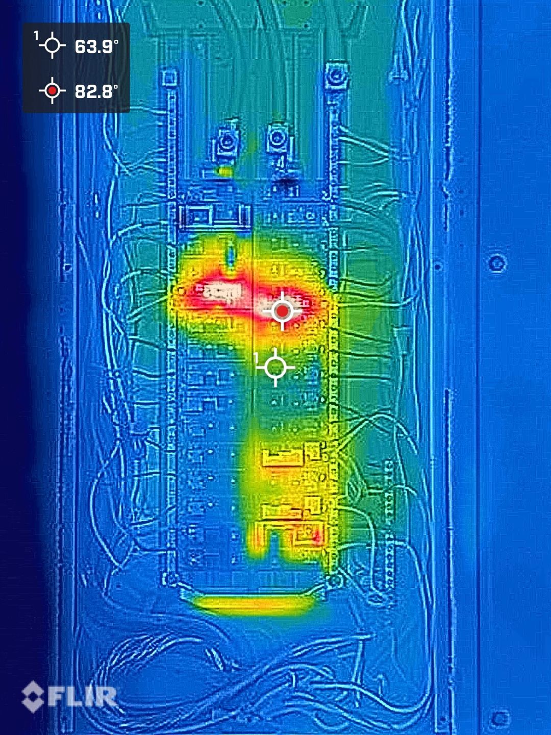 FLIR thermal image of an electrical panel with a hot red/yellow component in the center