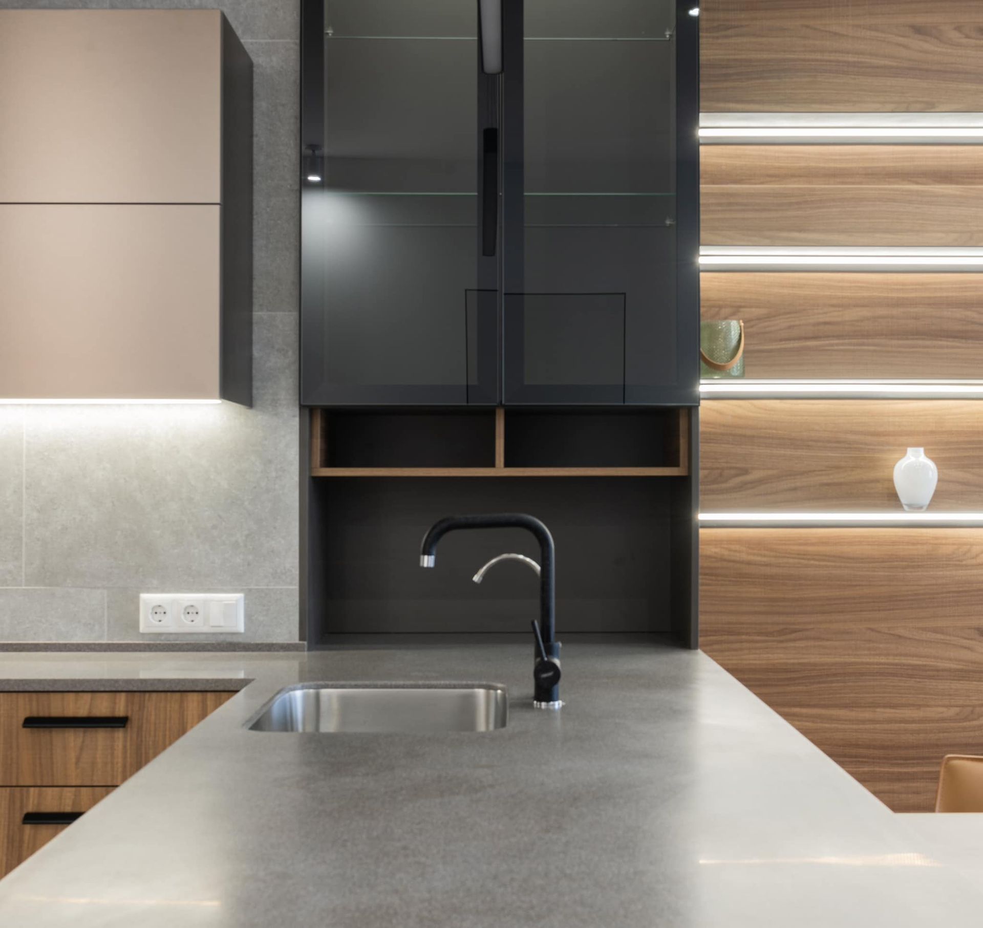 Modern kitchen with dark cabinetry, stainless steel sink, wood shelving, and light gray countertops.