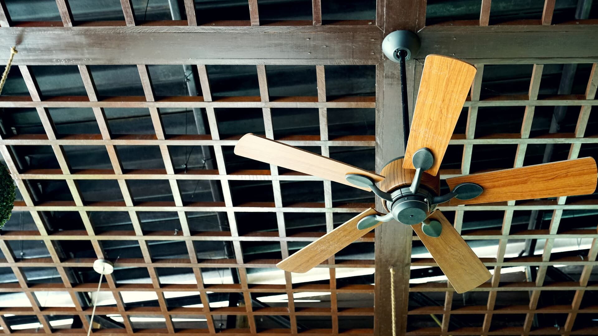 Ceiling fan with wooden blades, hanging below a latticed wooden ceiling.