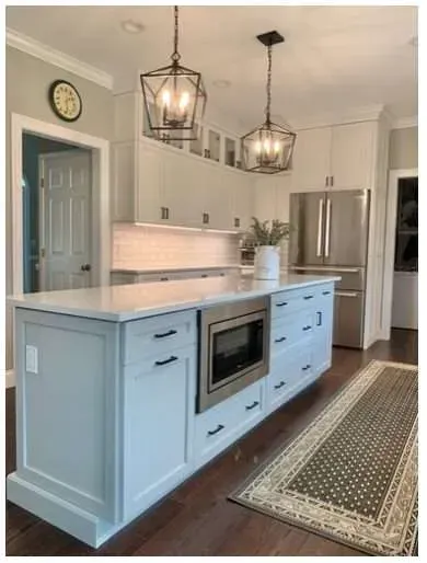 A modern kitchen island with light blue cabinets and a built-in microwave, set in a room with white cabinets and decor.