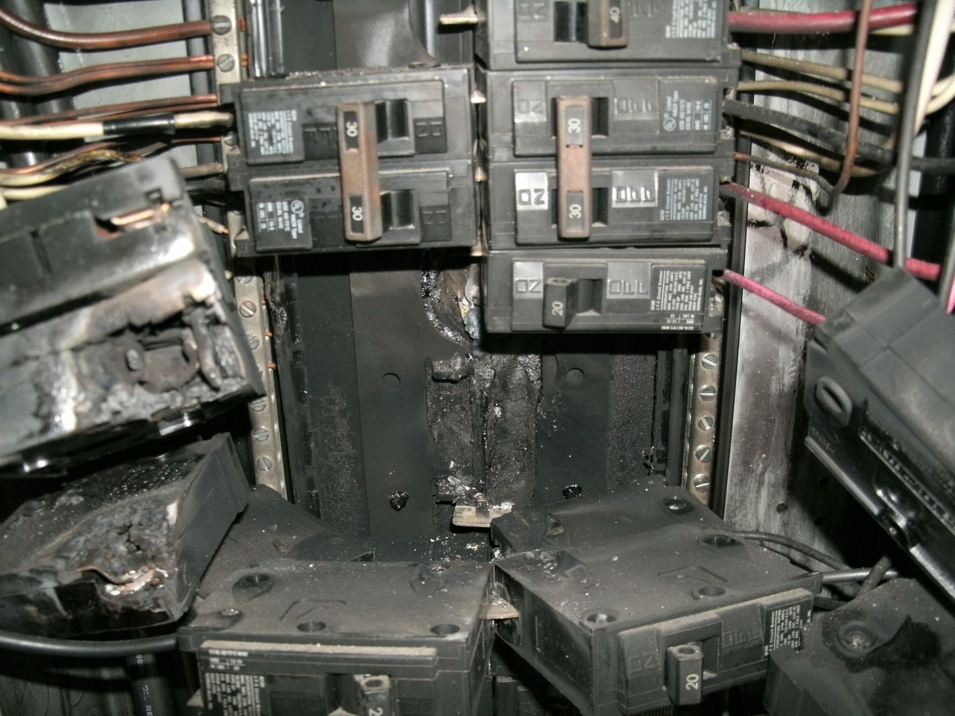 Burned electrical breaker panel with melted wiring and soot damage