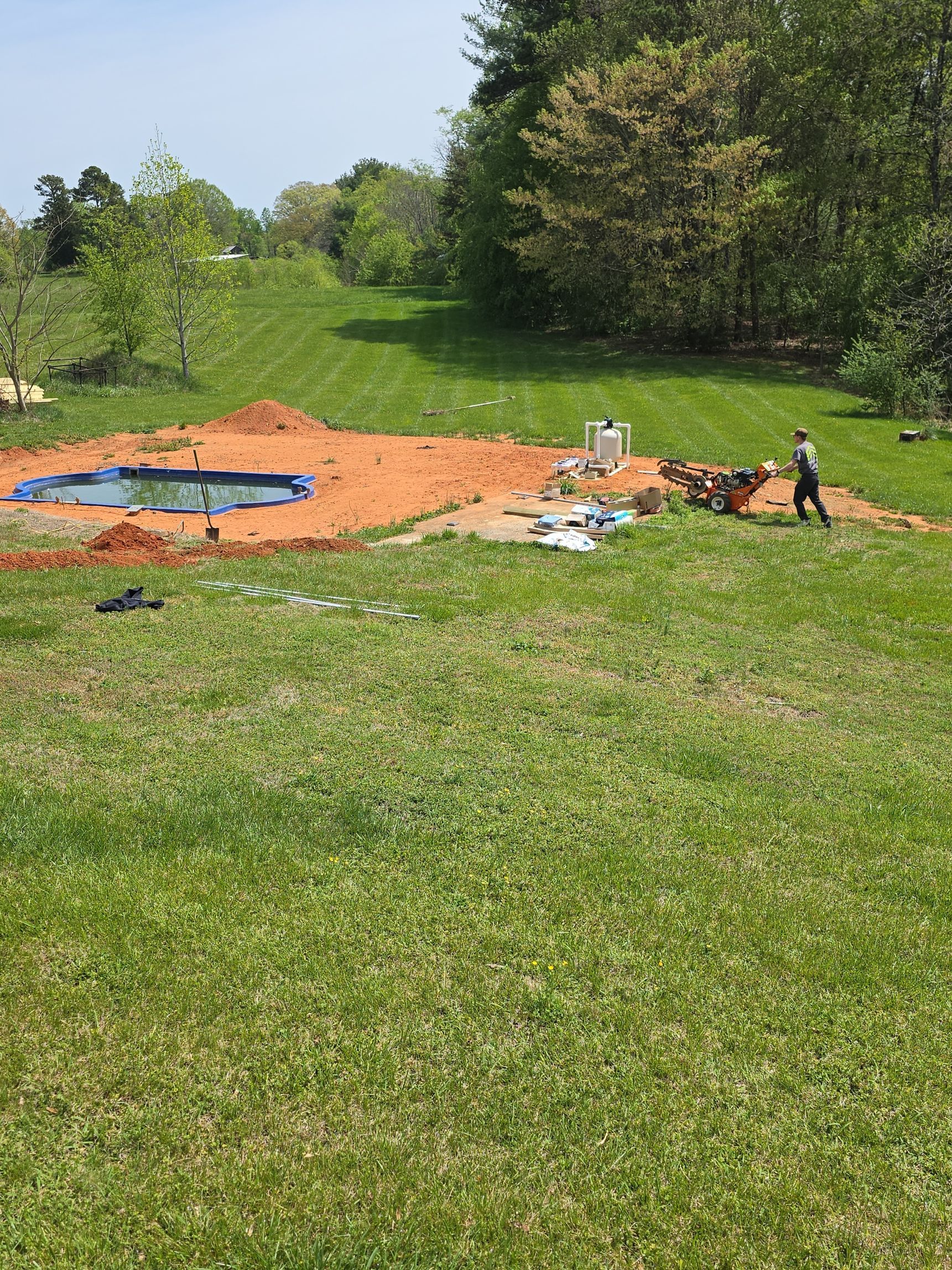 Circular blue pool on orange tarp in a grassy field, with scattered debris and trees in the background