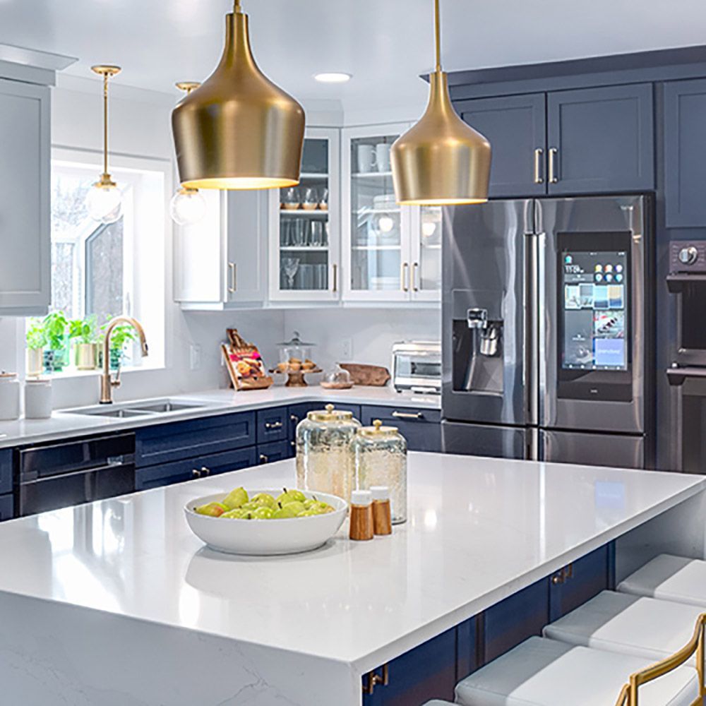 Modern kitchen with white island, navy cabinets, gold pendant lights, and stainless steel appliances