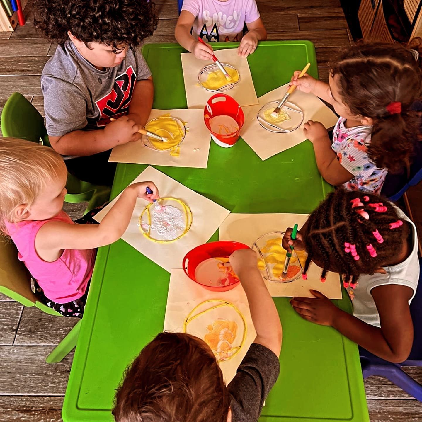 A group of children are sitting around a green table painting