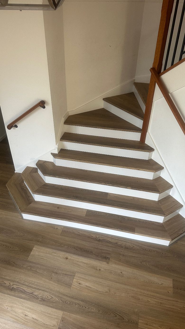 Staircase with brown steps, white risers, and a wooden handrail, leading to an upper level.