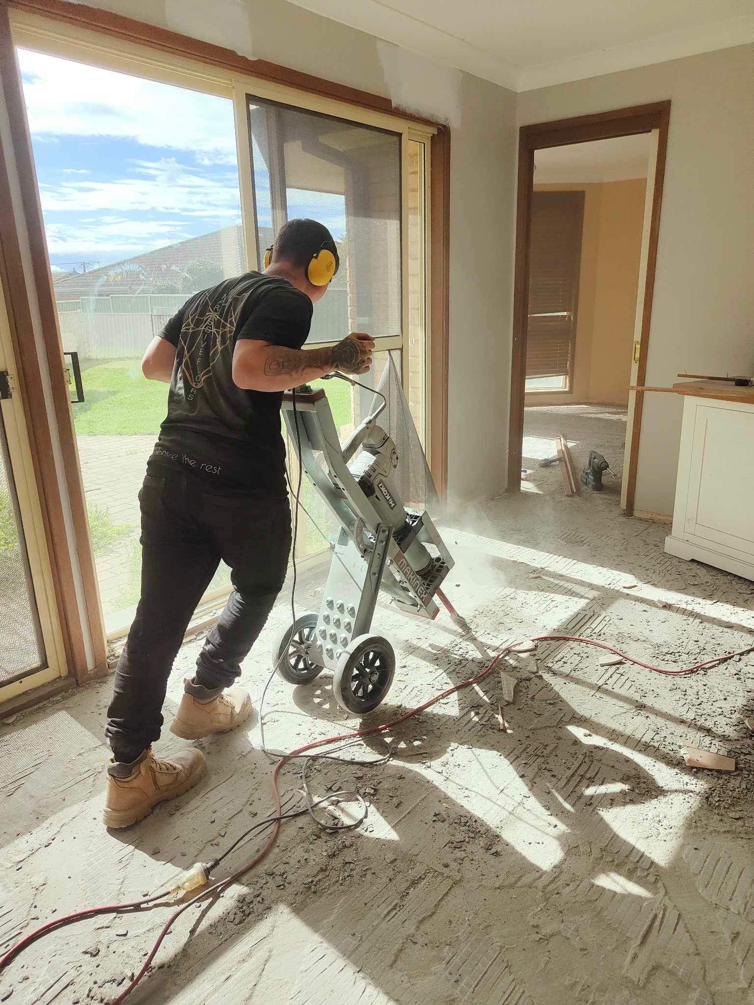 A construction worker uses a saw to cut flooring indoors, generating dust.