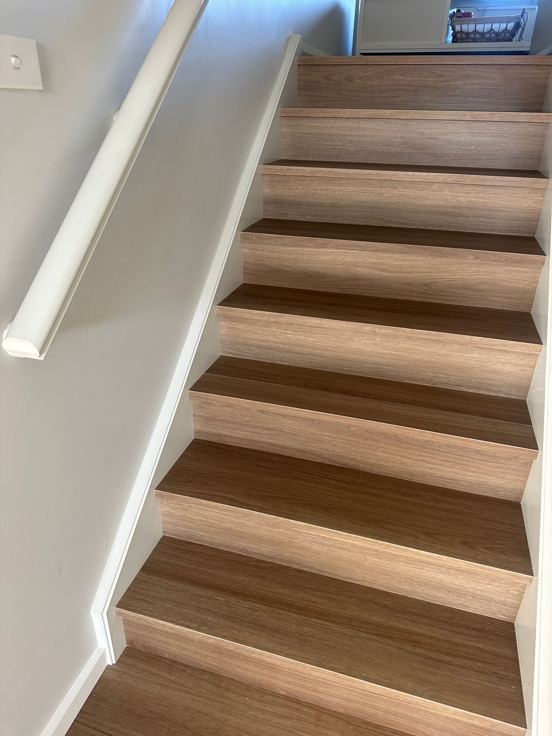 Wooden stairs with white risers, a white handrail on the left side, and a white wall.