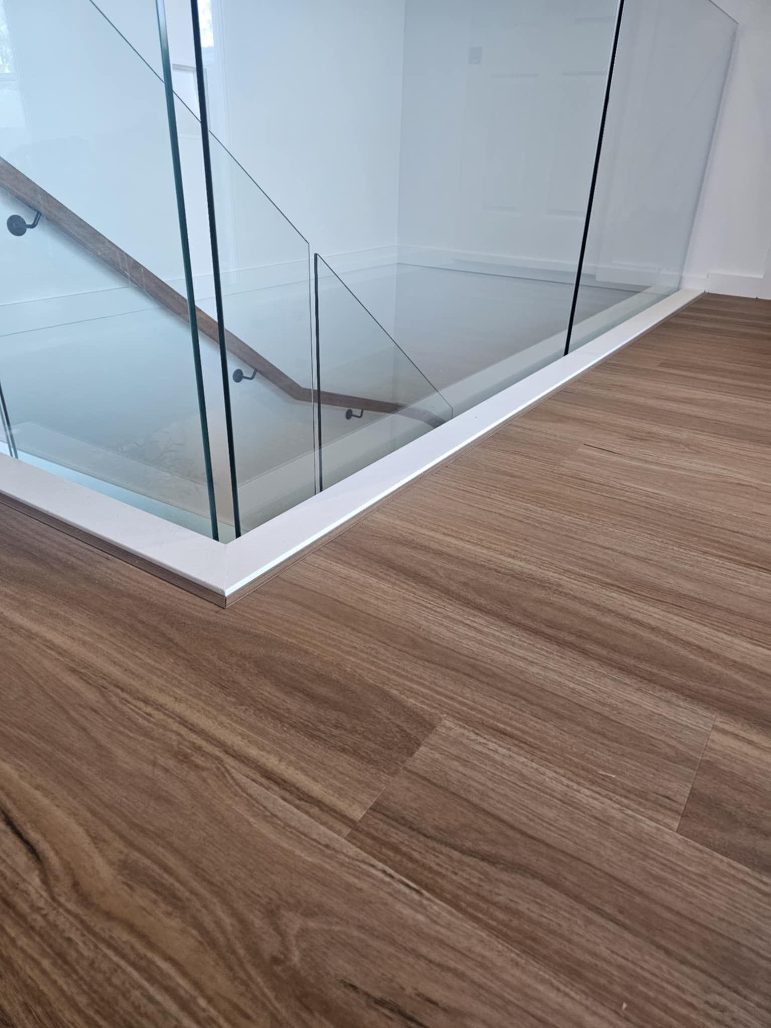 A staircase with a wooden floor and a glass railing.