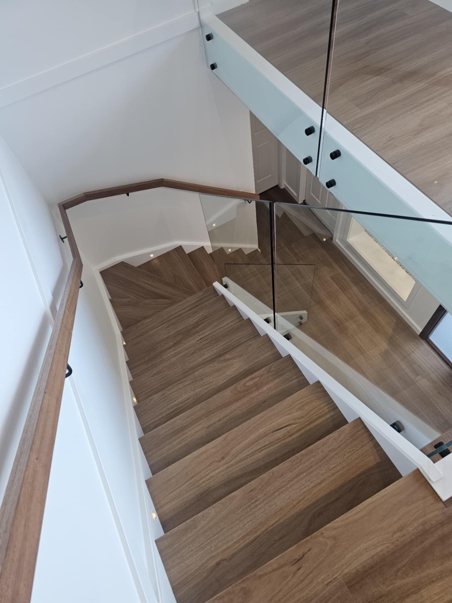 A wooden staircase with a glass railing and a wooden handrail.