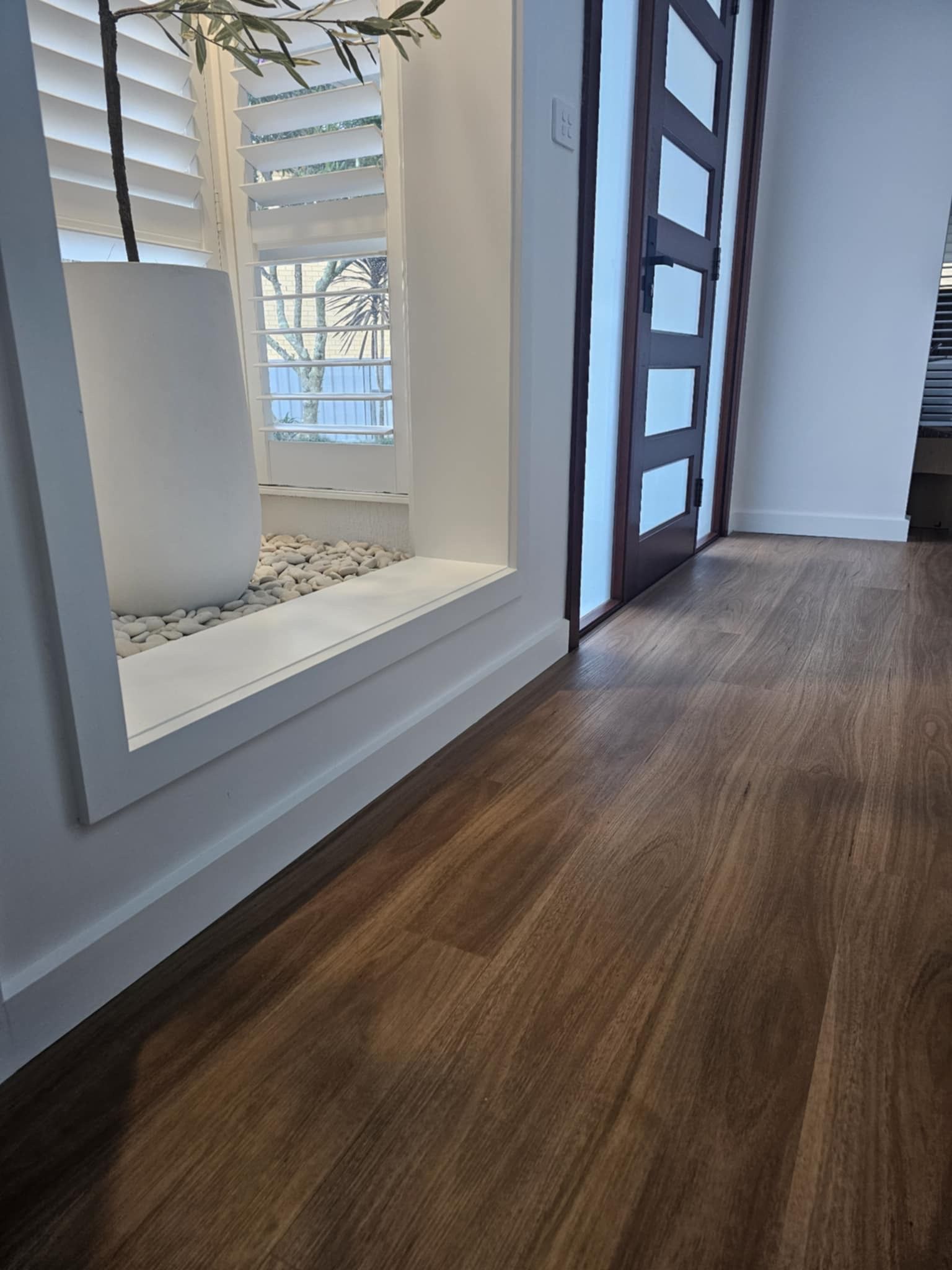 A hallway with a wooden floor and a window with shutters.