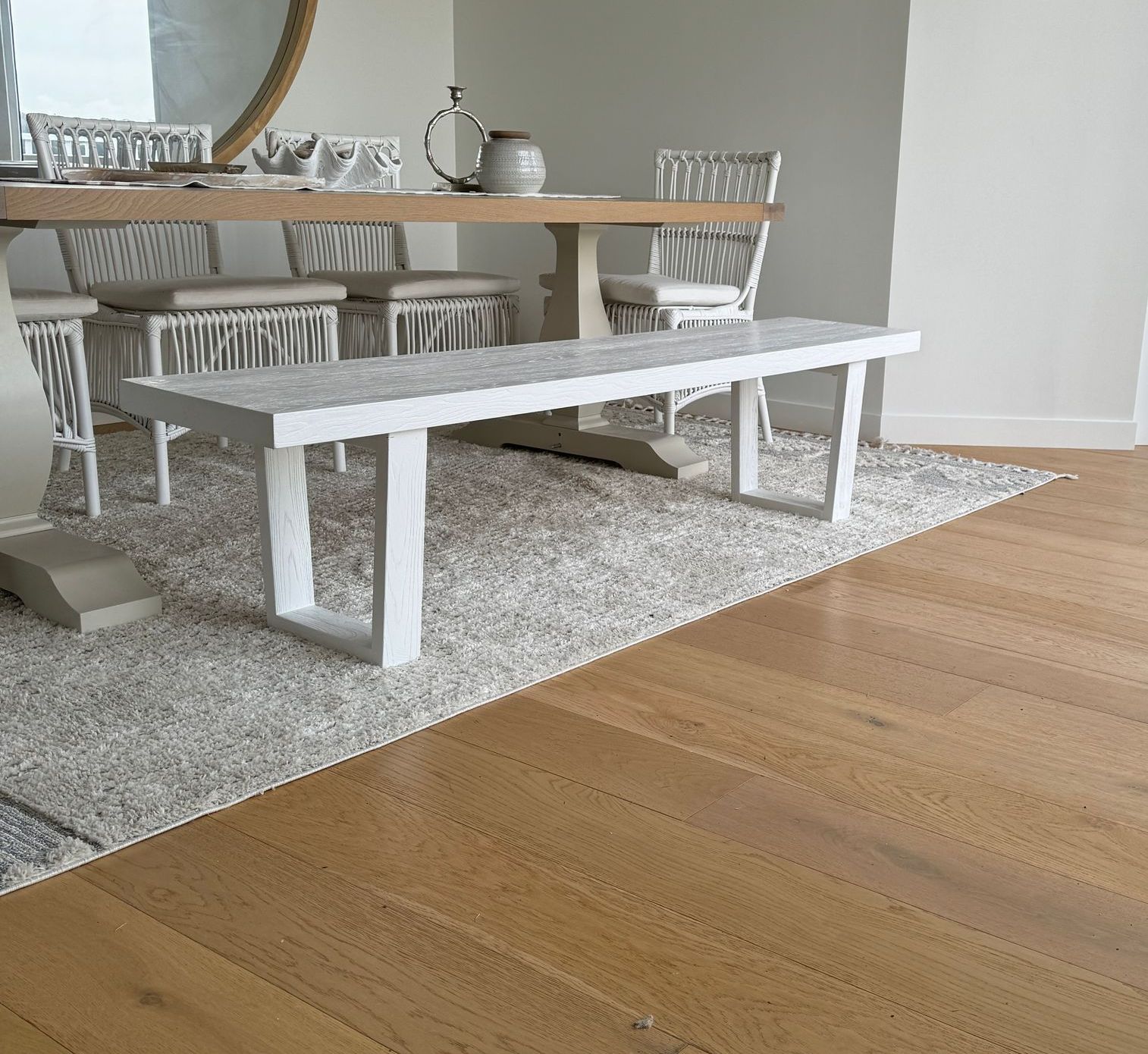 Dining room with light wood floor, textured rug, white table, and chairs.