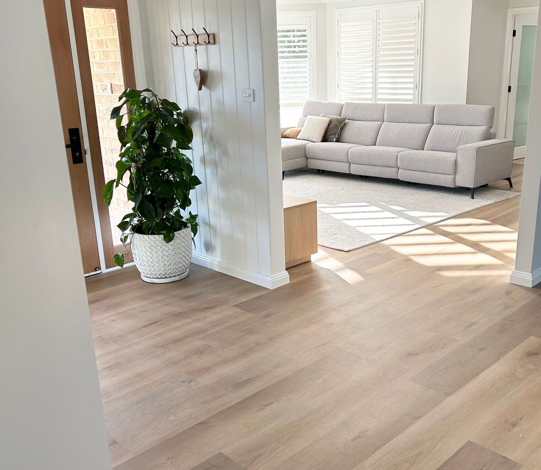 Light wood floor leads to a living room with a couch and a plant.