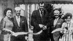 Ribbon-cutting ceremony with five people holding a ribbon in front of a building.