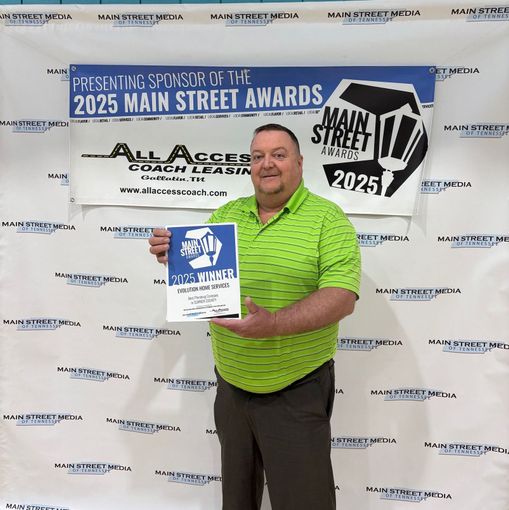 Man holding an award, standing in front of a banner for the 2025 Main Street Awards, sponsored by All Access Coach Leasing.