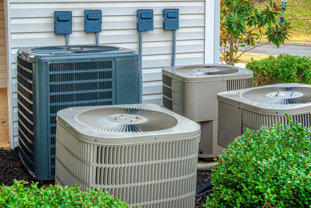 Several outdoor air conditioning units near a building, with electrical boxes above.