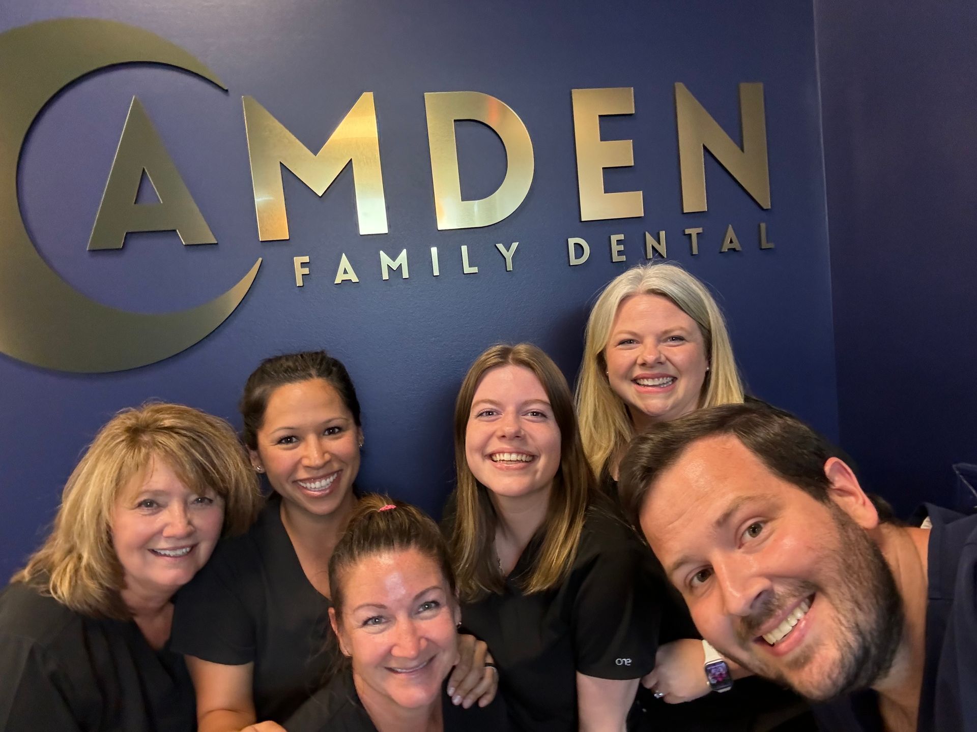 A group of people are posing for a picture in front of a sign that says amden family dental.