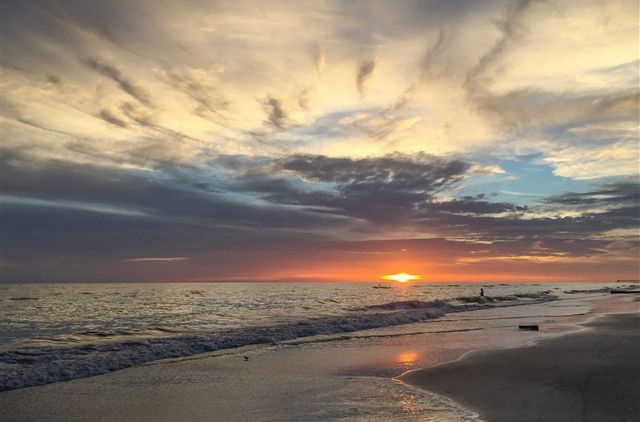 Sunset over a calm beach with waves, glowing orange horizon, and dramatic clouds.