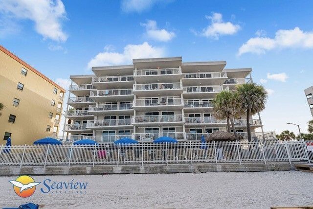 Beachfront Seaview condominium with balconies, blue umbrellas, and a palm tree behind a seawall
