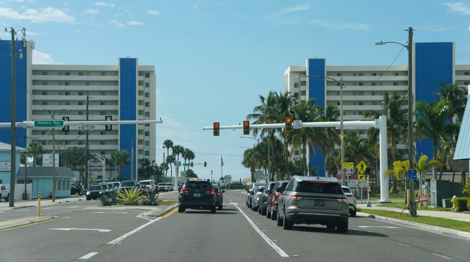 Busy city street with cars approaching a traffic light, flanked by tall office buildings and palm trees