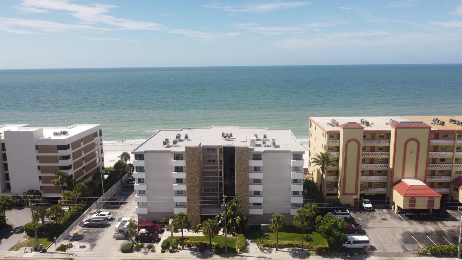 Oceanfront apartment buildings with balconies and a calm blue sea in the background.